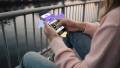 Person in rosanem Hoodie und Jeas hält in ihrer rechten Hand ein Smartphone mit der Startseite von „JUP!“.