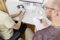 Zwei UXMA-Mitarbeiter sitzen an einem Schreibtisch. Einer notiert mit Kugelschreiber auf einem Notizblock. Die andere bedient die Home Connect Plus App auf einem Smartphone.