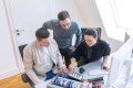 Drei Personen sitzen an einem Tisch und sprechen gemeinsam über eine Computer Hardware.