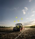 A tractor plows a field. Various icons are displayed above it, indicating different functions. The field is divided into squares with white lines.