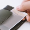 Close-up photo of the packaging. A hand removing a card-shaped product from a leather sleeve.