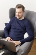 A UXMA employee sitting comfortably in a wing chair reading on his laptop.