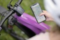 Bicycle with bike computer on the handlebars. In front of it, a hand holding a smartphone with a map app open showing a route.