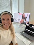 A woman with a headset sits in front of a computer and laughs into the camera. Her screen reads: "Positive psychology: you can learn to be happy!"