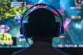 Man with headset from behind. In front of him is a blurred image of a screen on which a video game is being played.