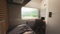 In the rendered interior view of the cabin, a large window with integrated projections of the route can be seen. There is also a desk, a chair and a bed in the picture section. An interplay of different materials, wood and felt can be seen.